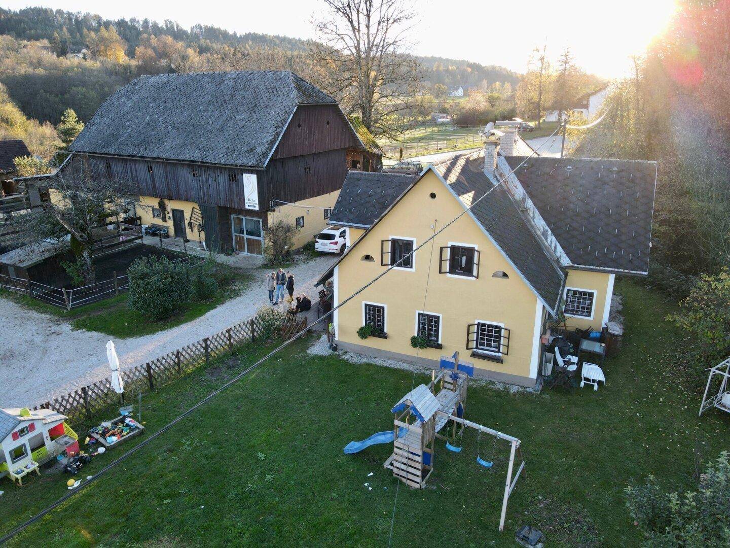 Nahaufnahme des gelben Hauses und der Scheune von oben, mit Spielplatz im Gartenbereich.