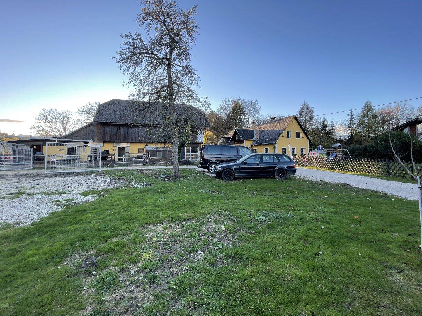 Geräumiger Schotterparkplatz vor dem Anwesen mit dem gelben Haus und der Scheune im Hintergrund.