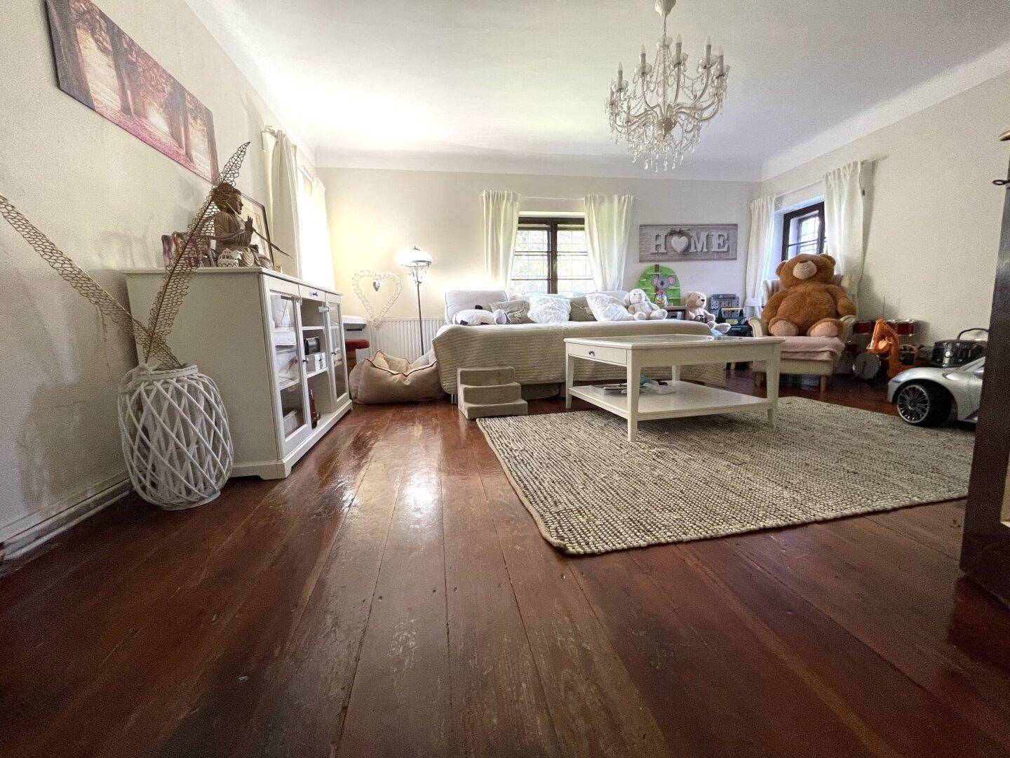 Geräumiges Wohnzimmer mit Holzboden, Kronleuchter und gemütlicher Einrichtung.