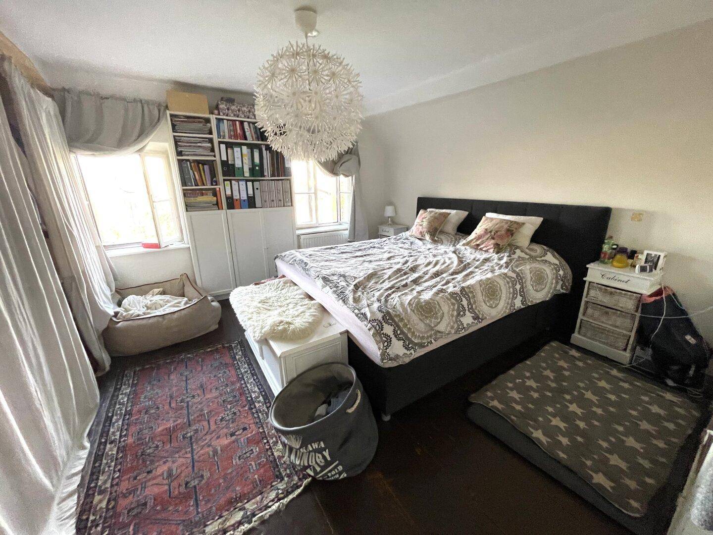 Gemütliches Schlafzimmer mit Holzboden, großem Bett und Bücherregal.