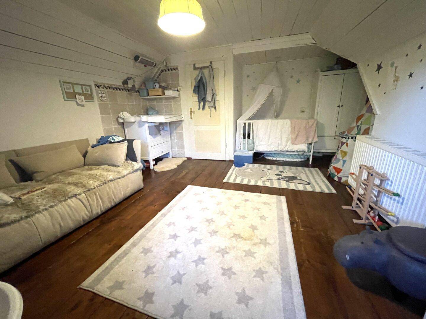 Kinderzimmer im Dachgeschoss mit Holzboden, Dachschräge und Babybett.