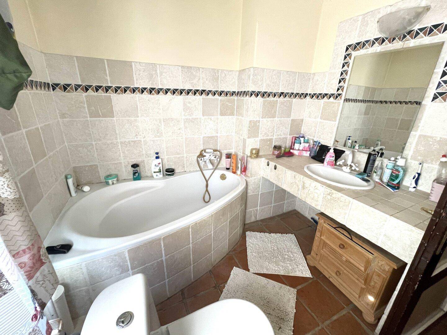 Badezimmer mit Eckbadewanne, Fliesen und großem Spiegel.
