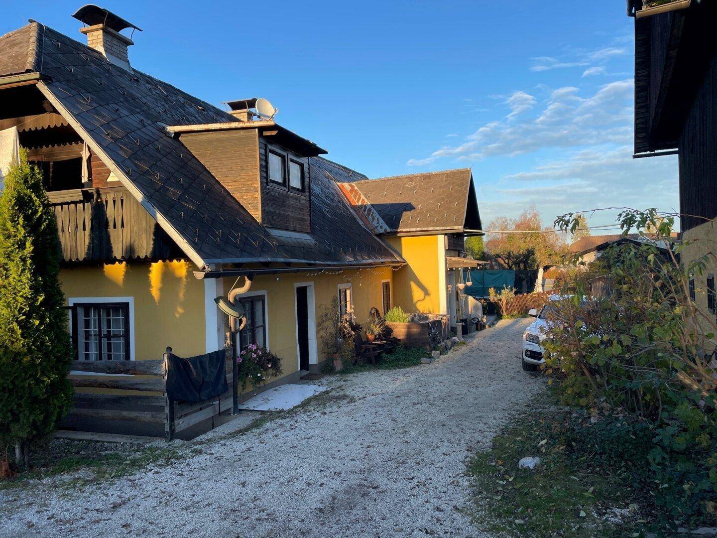 Seitenansicht des traditionellen gelben Hauses mit Schotterweg und üppiger Vegetation im Vordergrund.