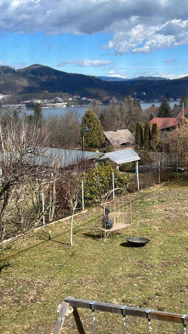 Gartenbereich mit Rasenfläche und Blick auf den See sowie die umliegenden Berge unter bewölktem Himmel.