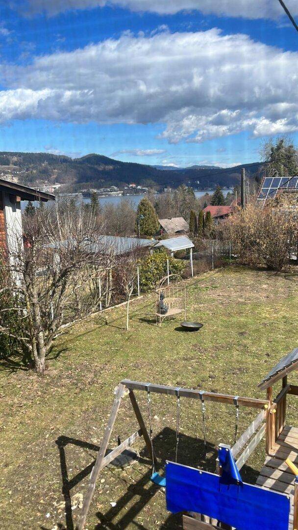 Garten mit Spielgeräten und weitem Blick auf den See und die bewaldeten Berge in der Ferne.