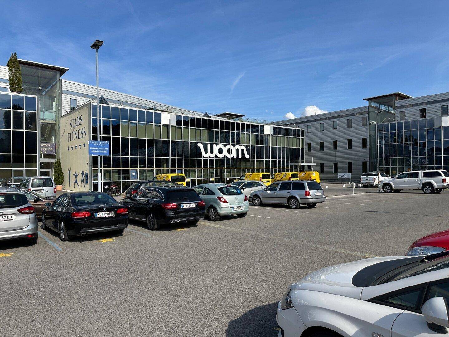 Modernes Geschäftsgebäude mit großer Glasfassade und einem Parkplatz davor.