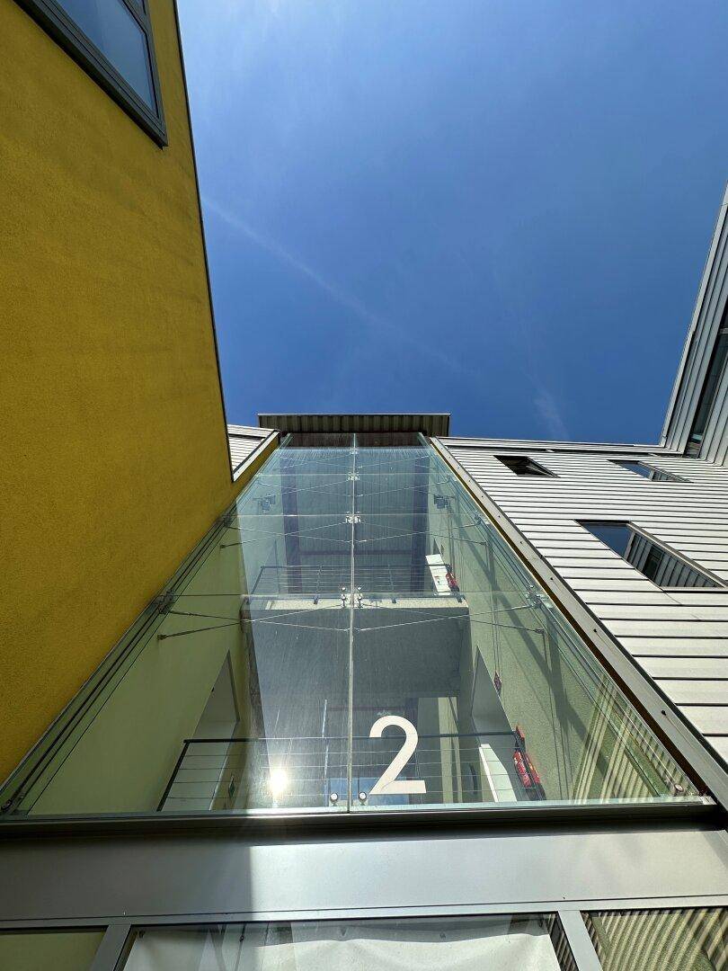 Blick nach oben auf eine moderne Glasfassade und die Architektur des Gebäudes unter blauem Himmel.