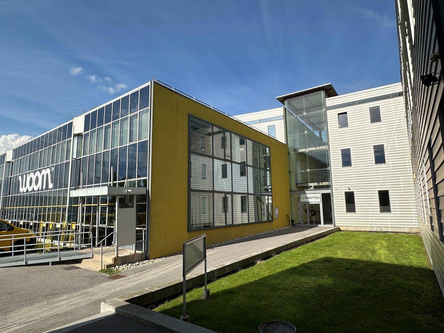Modernes Geschäftsgebäude mit Glasfassade, Rampe und gepflegter Grünfläche.