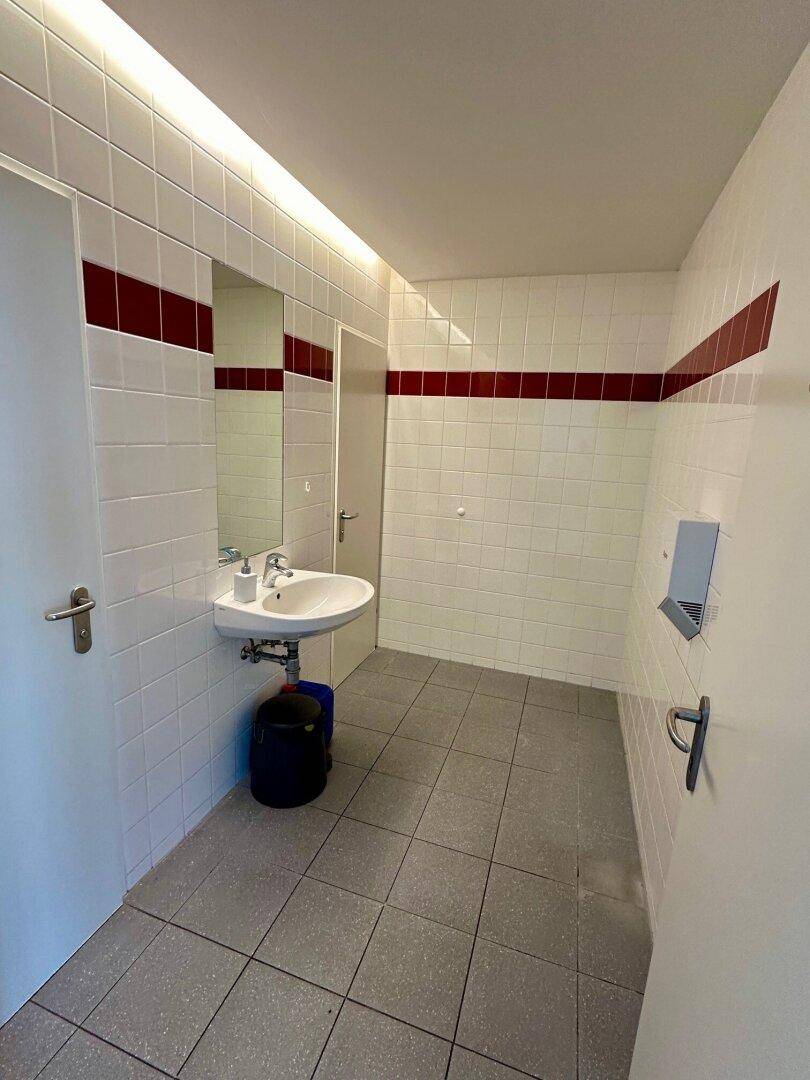 Badezimmer mit weißen Fliesen, rotem Akzentstreifen, Waschbecken und Spiegel.