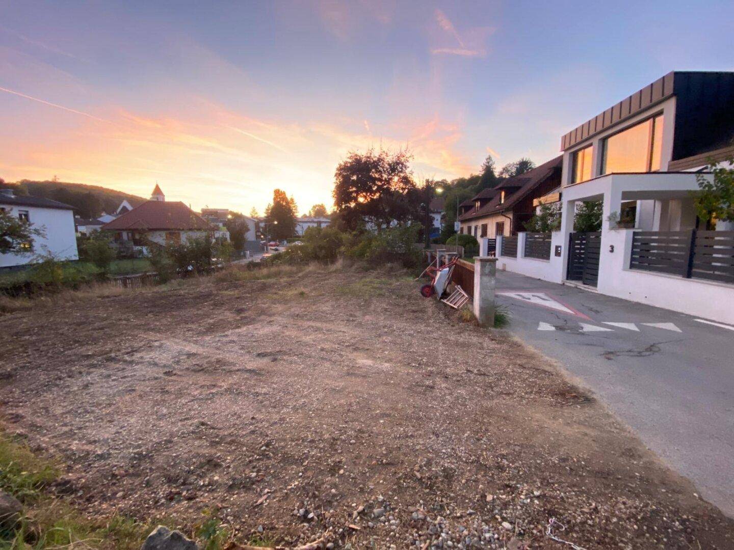 Leeres, geräumtes Grundstück bei Sonnenuntergang, angrenzend an ein modernes Wohnhaus.