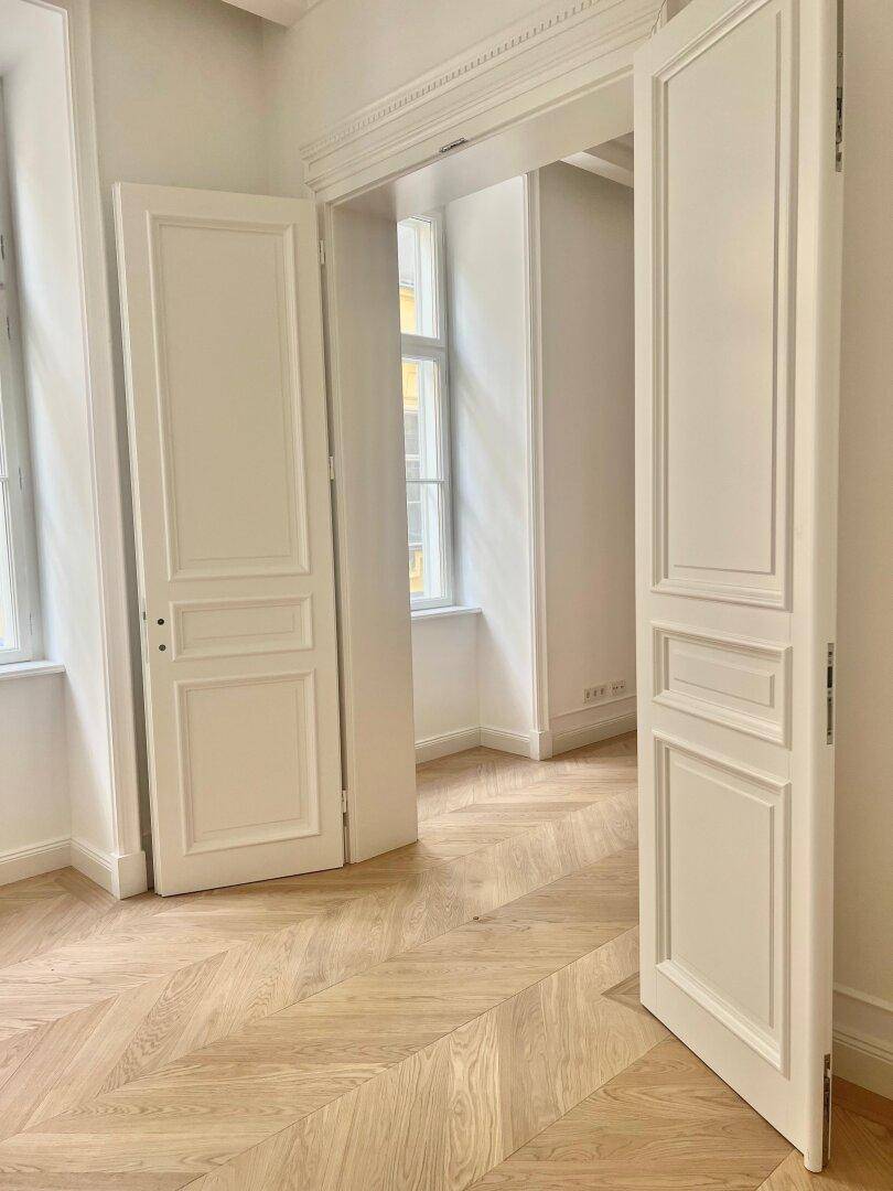 Eleganter Flur mit Fischgrätparkett und hohen Flügeltüren, der verschiedene Räume verbindet.