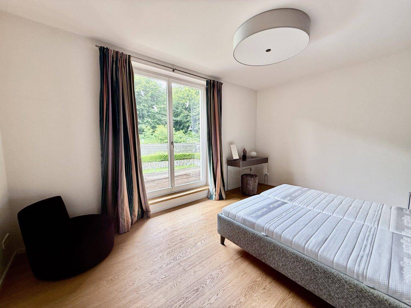 Helles Schlafzimmer mit Holzboden, Bett und großem Fenster mit Zugang zum Außenbereich.