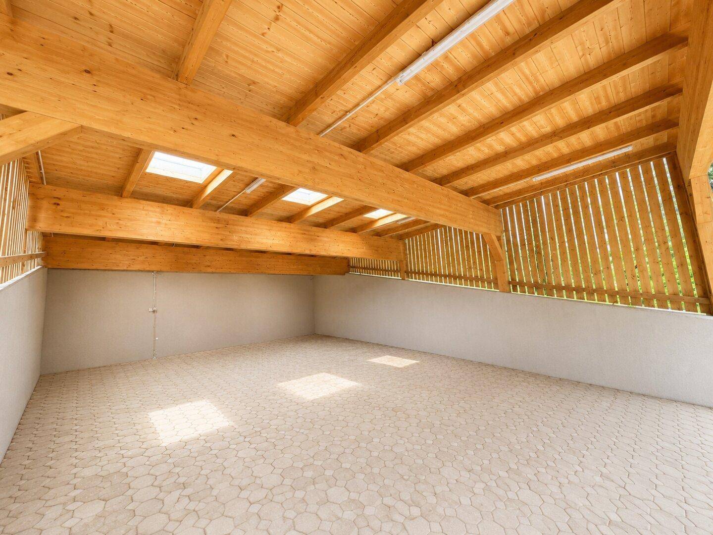 Geräumiger Raum mit hoher Holzdecke, sichtbaren Balken und Oberlichtern, ideal als Werkstatt oder Lager.