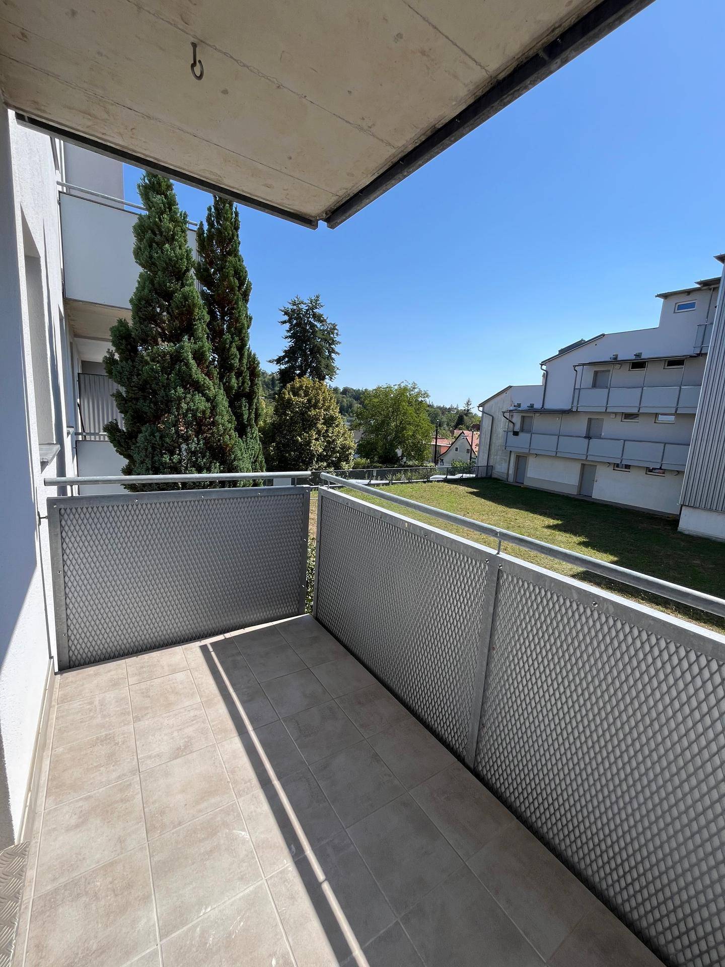 Langer Balkon mit Fliesenboden und Metallgeländer, umgeben von Grünflächen und Bäumen.