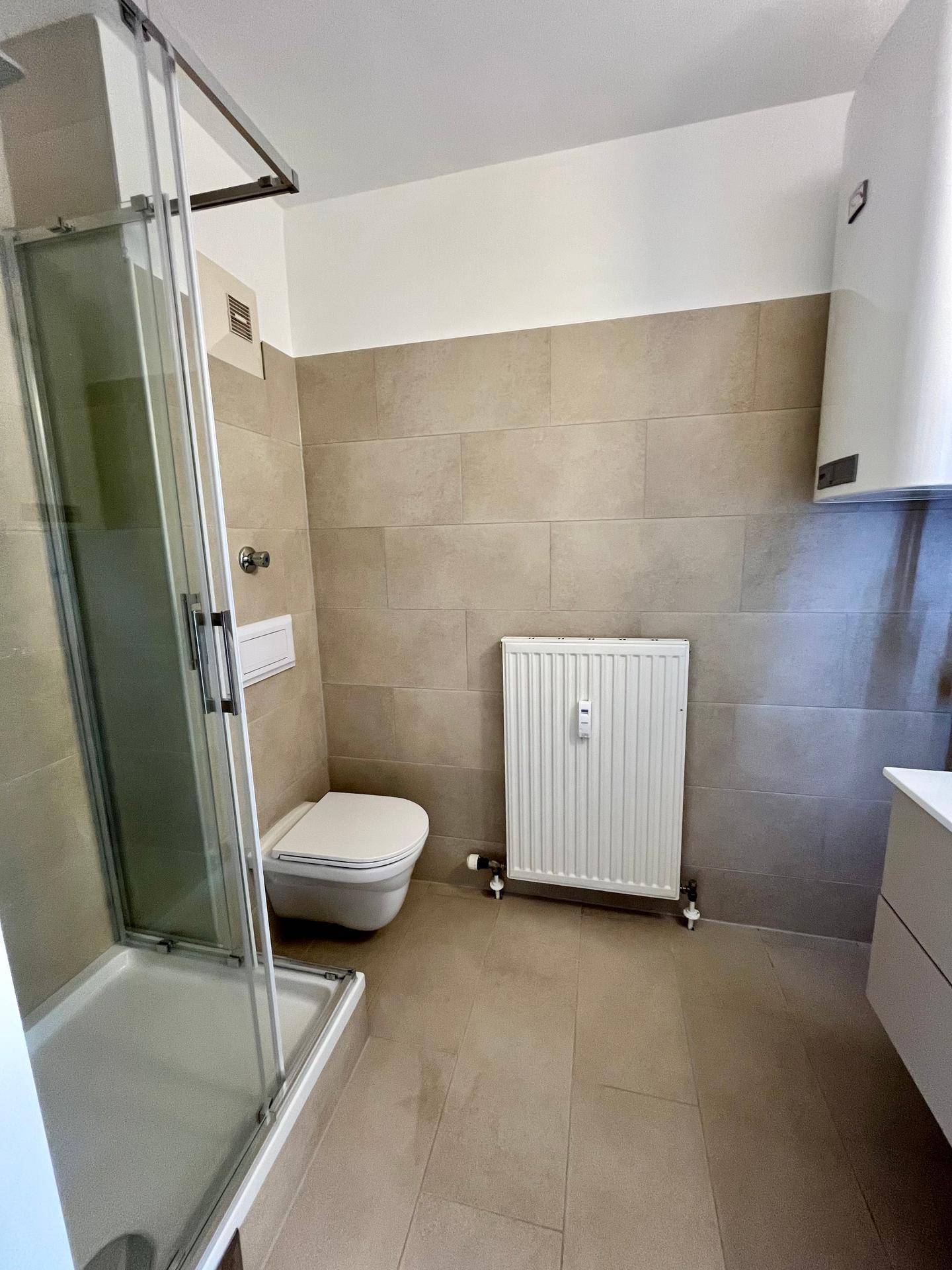Modernes Badezimmer mit beigefarbenen Fliesen, Duschkabine, wandhängendem WC und Heizkörper.