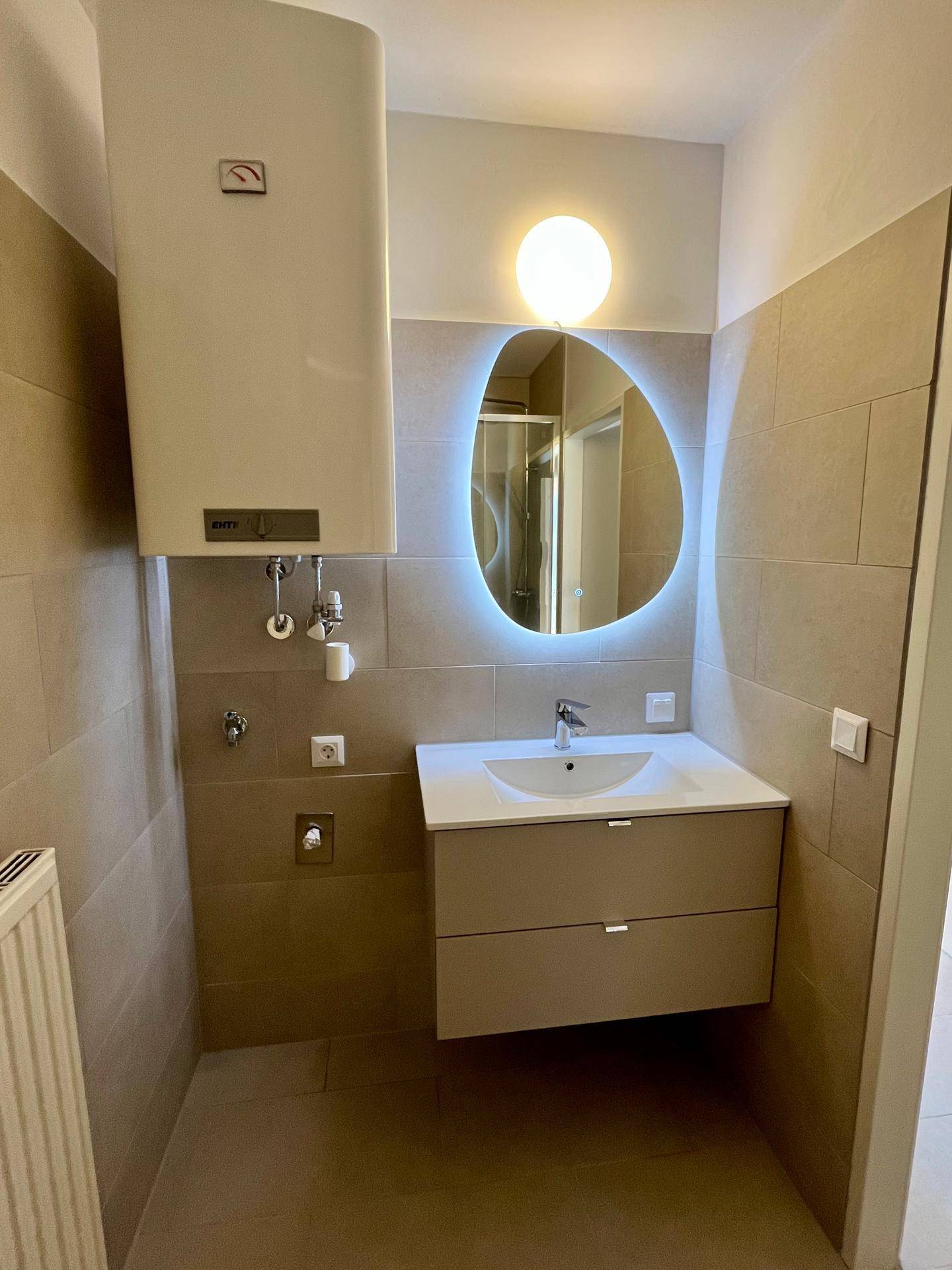 Badezimmer mit modernem Waschtisch, beleuchtetem Spiegel und beigefarbenen Wandfliesen.