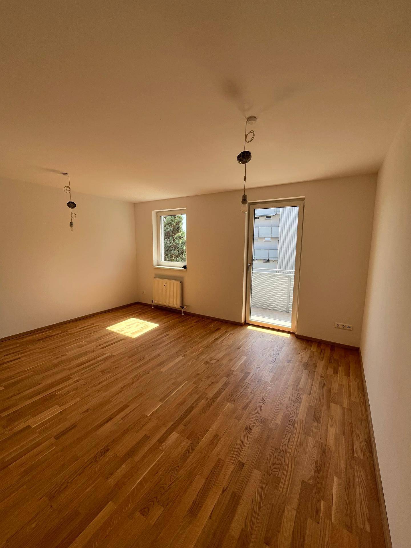 Helles Wohnzimmer mit Eichenparkettboden und Zugang zu einem Balkon, ideal für entspannte Stunden.
