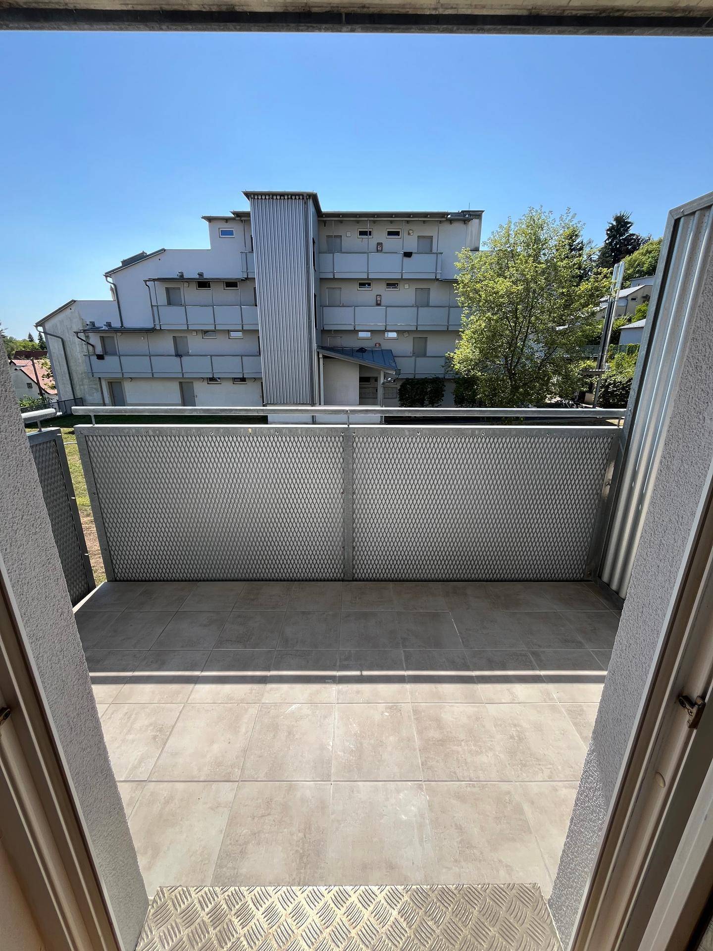 Balkon mit Fliesenboden und Metallgeländer, bietet Blick auf ein gegenüberliegendes Gebäude.