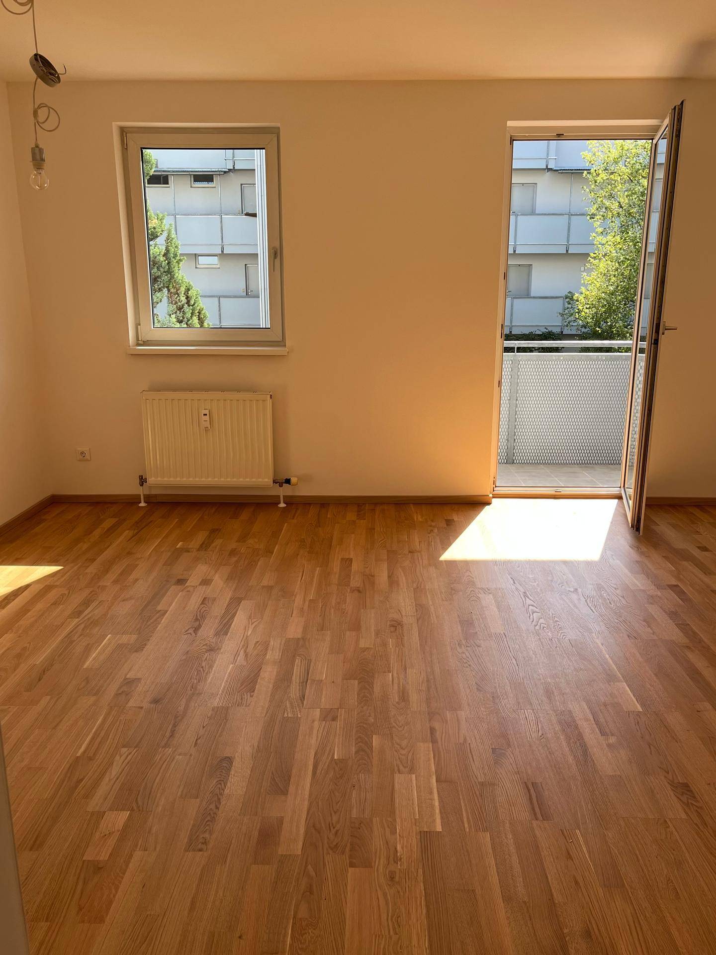 Lichtdurchflutetes Wohnzimmer mit Eichenparkett und Fensterfront, die den Blick auf die Umgebung freigibt.