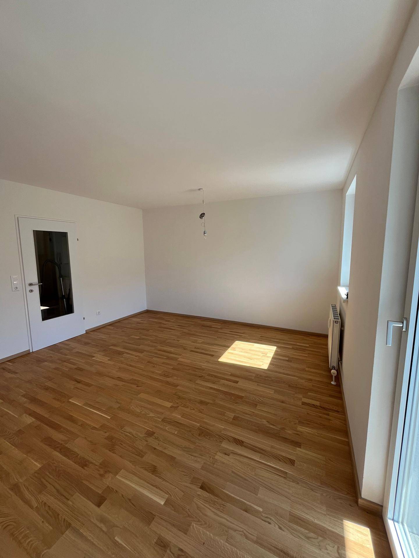 Geräumiges Wohnzimmer mit hellem Eichenparkett und großen Fenstern, die viel Tageslicht hereinlassen.