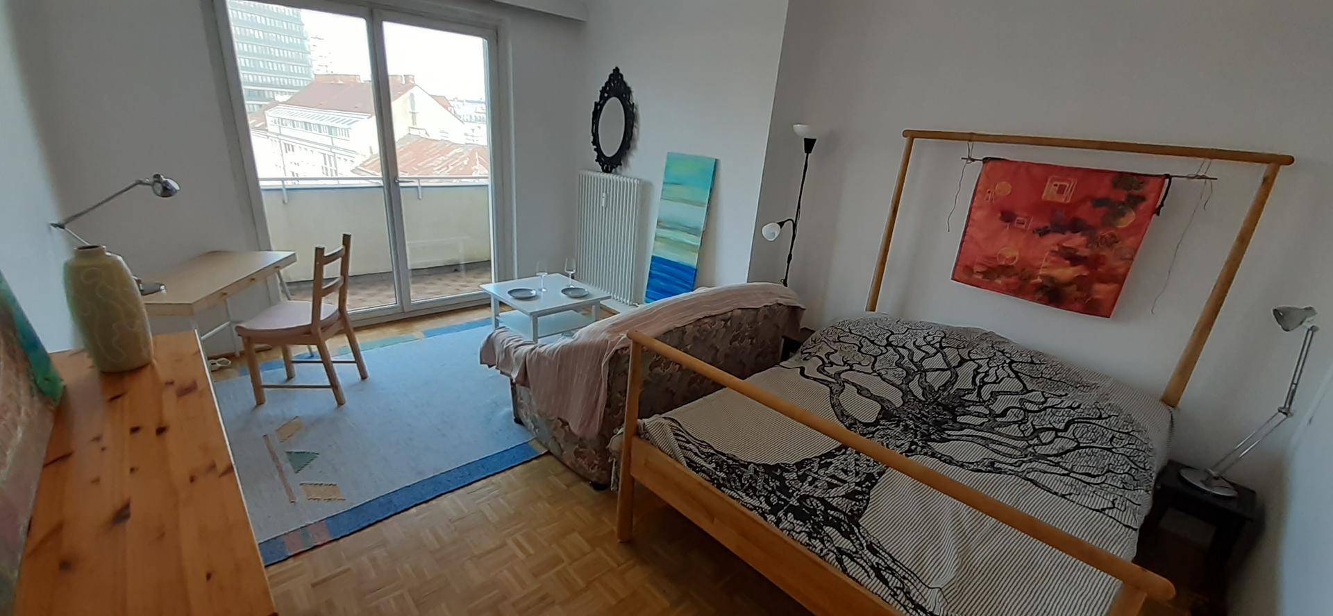 Helles Schlafzimmer mit Holzbett, Schreibtisch und Zugang zum Außenbereich.