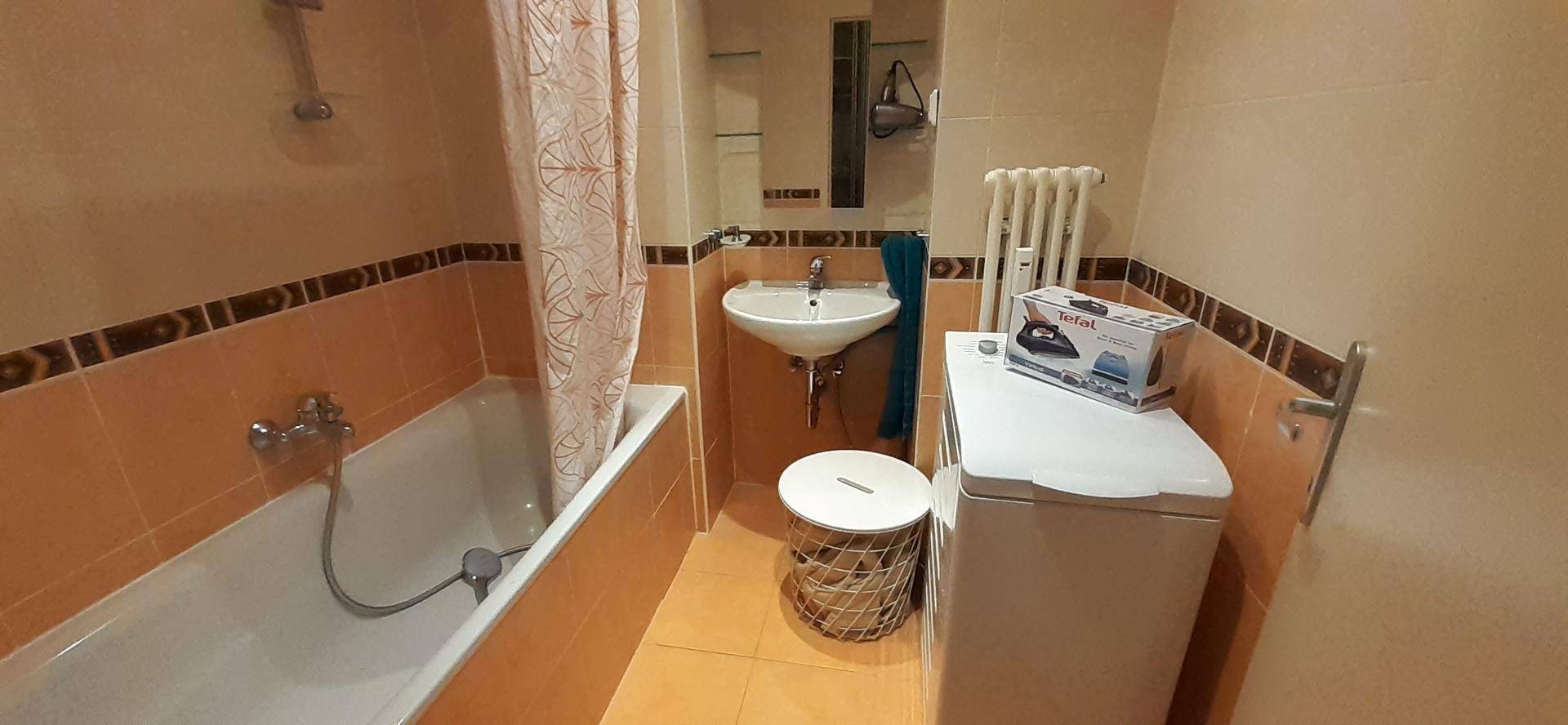 Badezimmer mit Badewanne, Waschbecken und Waschmaschine, in warmen Erdtönen gefliest.
