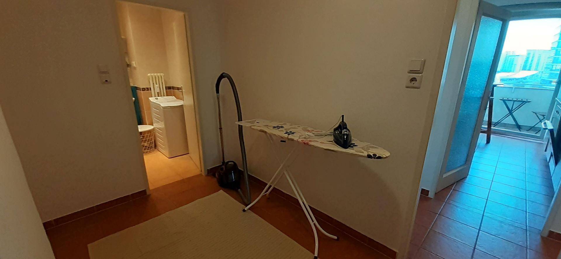 Praktischer Bereich mit Bügelbrett und Staubsauger, mit Blick auf den Balkon.