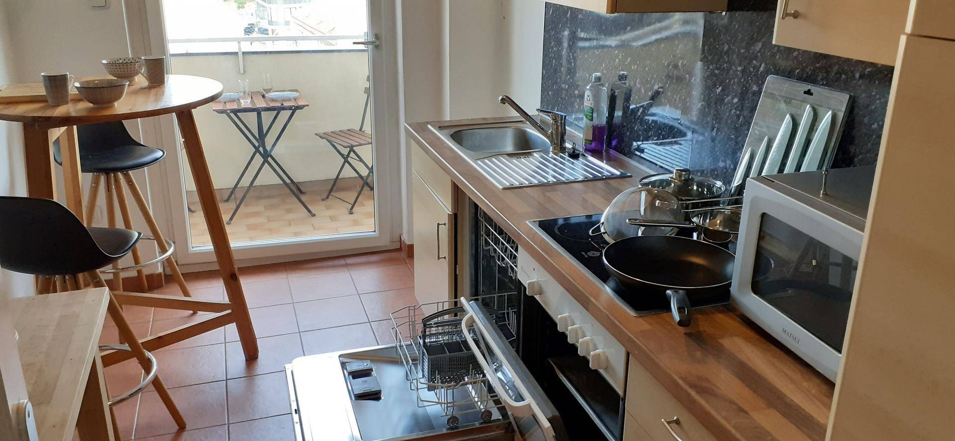 Funktionale Küche mit Spülmaschine, Kochfeld und Mikrowelle, direktem Zugang zum Balkon.