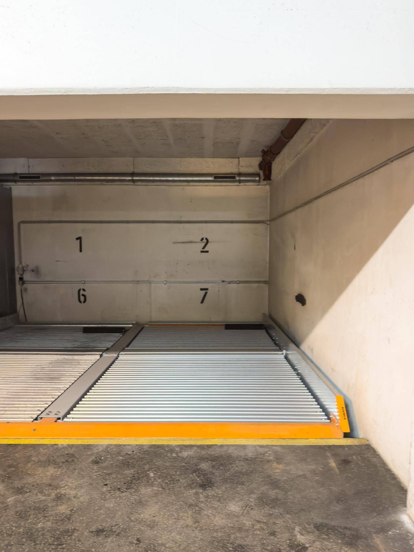 Mechanisches Doppelparkersystem in einer hell beleuchteten Tiefgarage mit nummerierten Stellplätzen.
