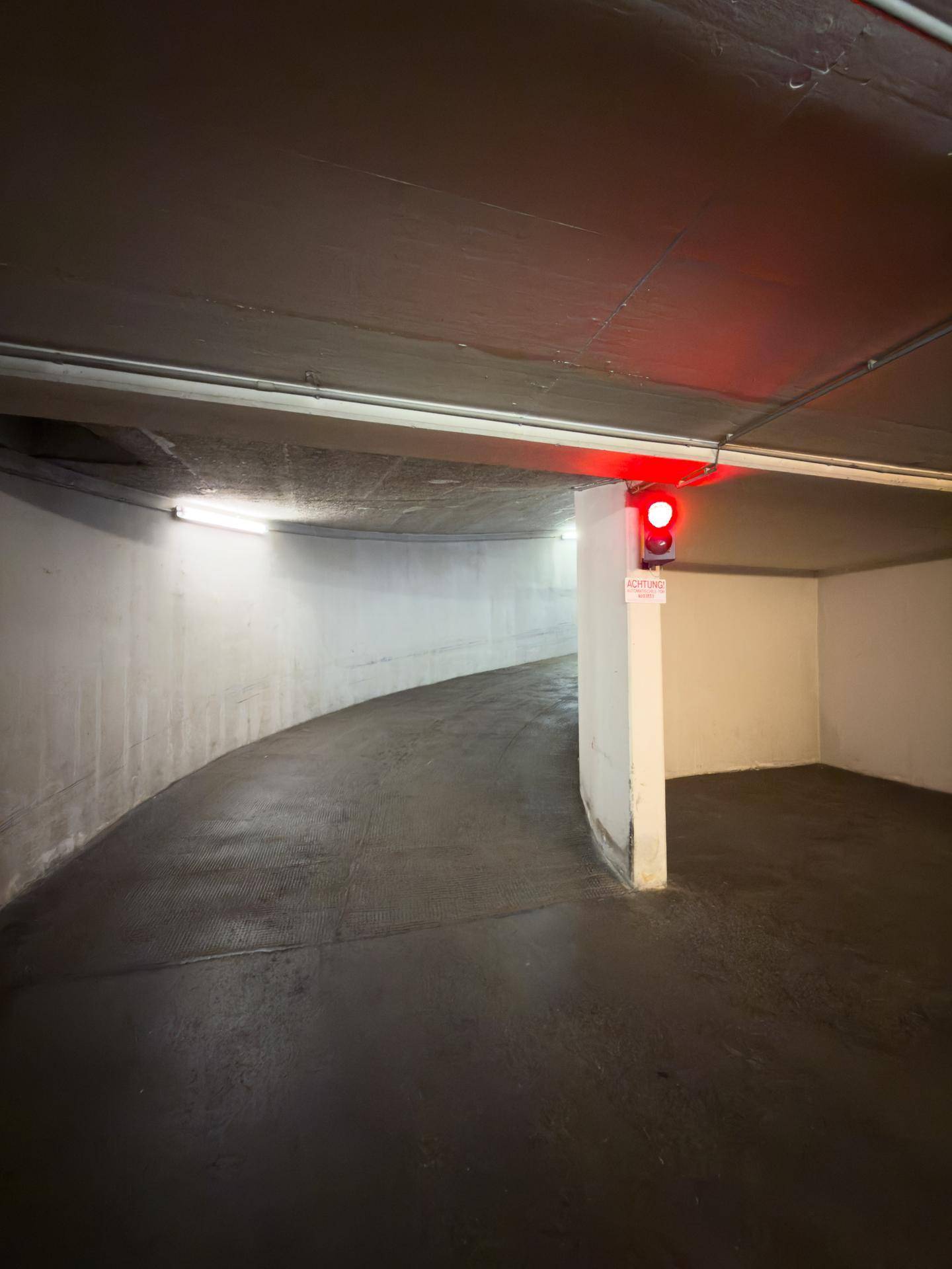 Kurvige Zufahrtsrampe zu einer Tiefgarage mit einem roten Verkehrssignal für die Einfahrtsregelung.