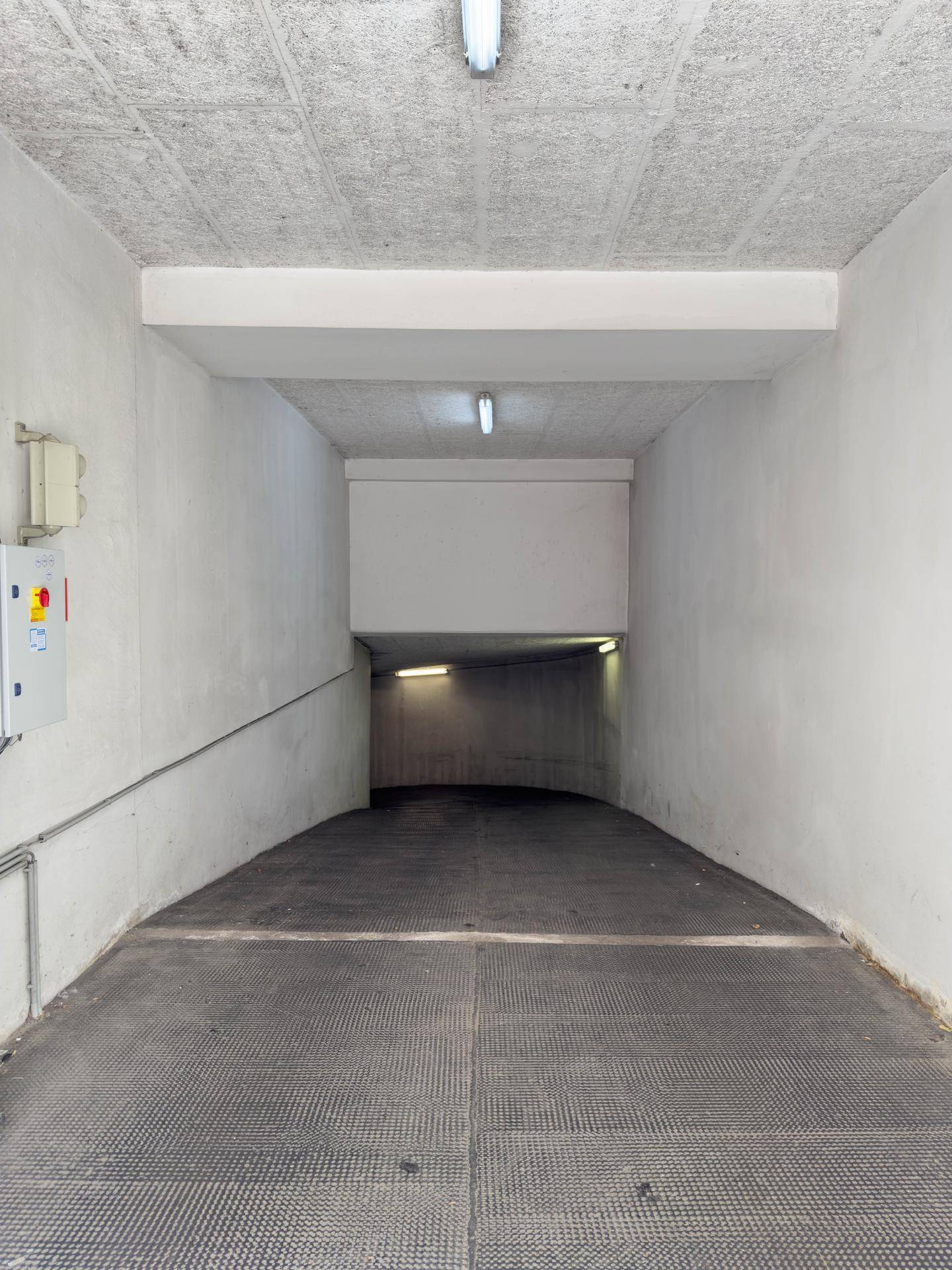 Gerader Zufahrtsweg zu einer Tiefgarage mit rutschfestem Bodenbelag und Beleuchtung für sichere Fahrt.