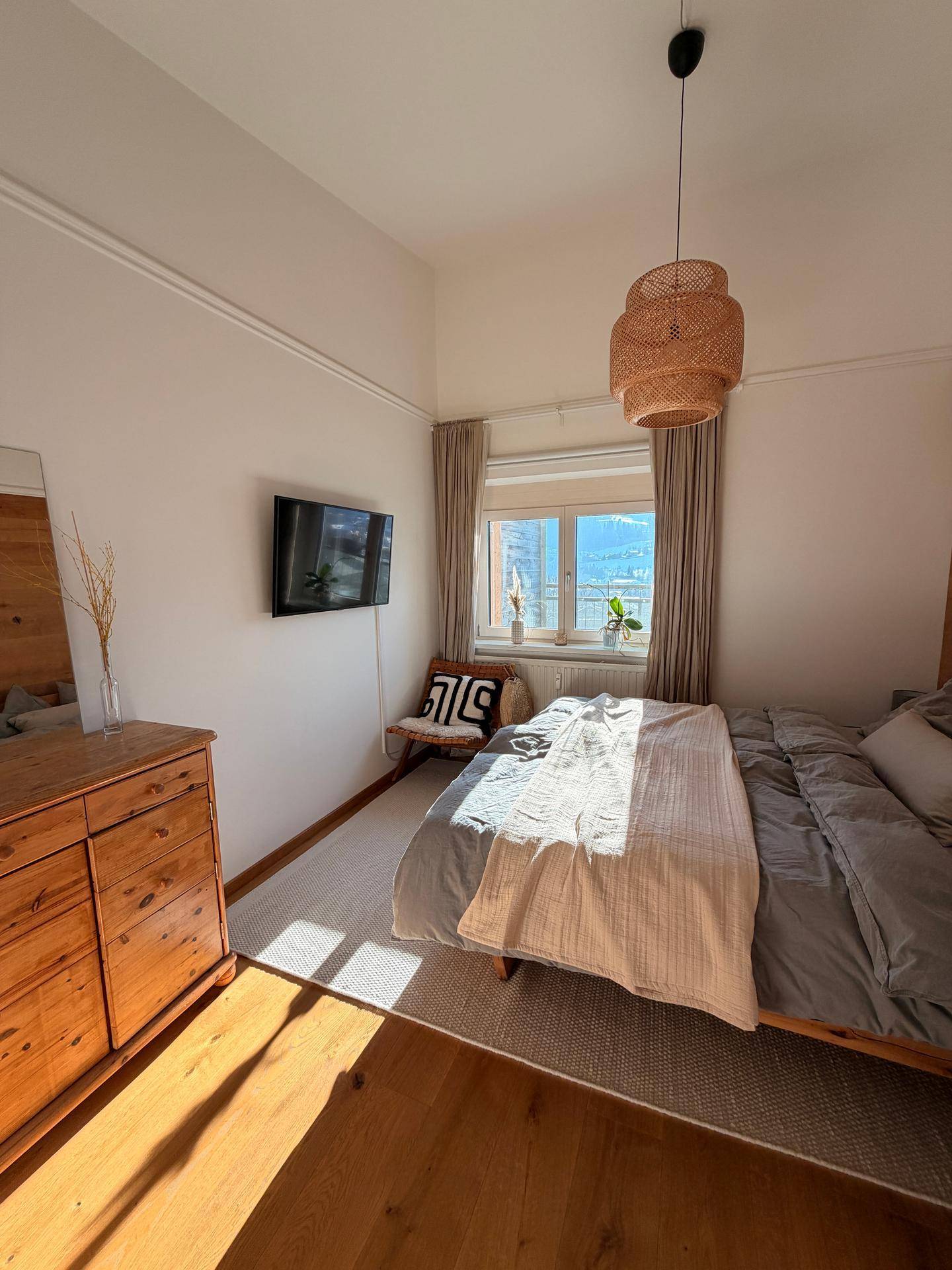 Helles Schlafzimmer mit Holzbett, Kommode und Blick auf die verschneite Landschaft.