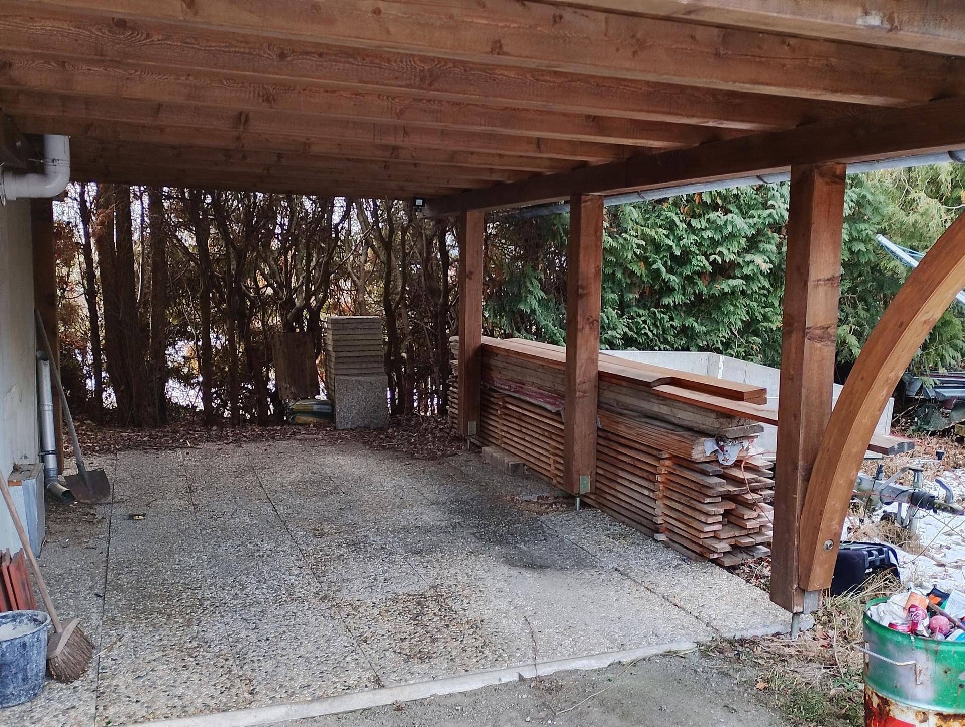 Überdachter Parkplatz oder Carport mit Holzkonstruktion und gelagertem Holz.