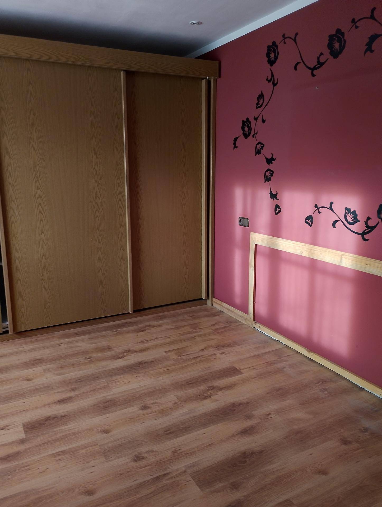 Schlafzimmer mit Laminatboden, großem Einbauschrank und einer rosa Wand mit floralem Dekor.