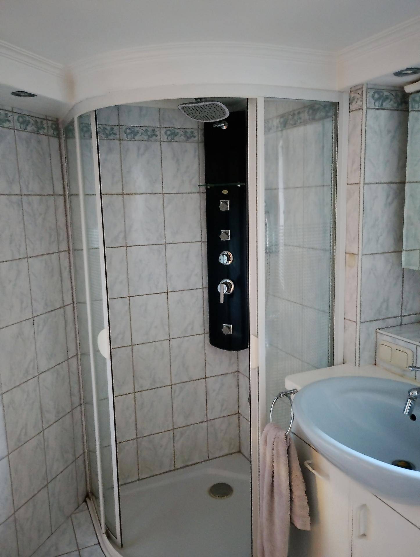 Badezimmer mit Duschkabine, gefliesten Wänden und einem Waschbecken.