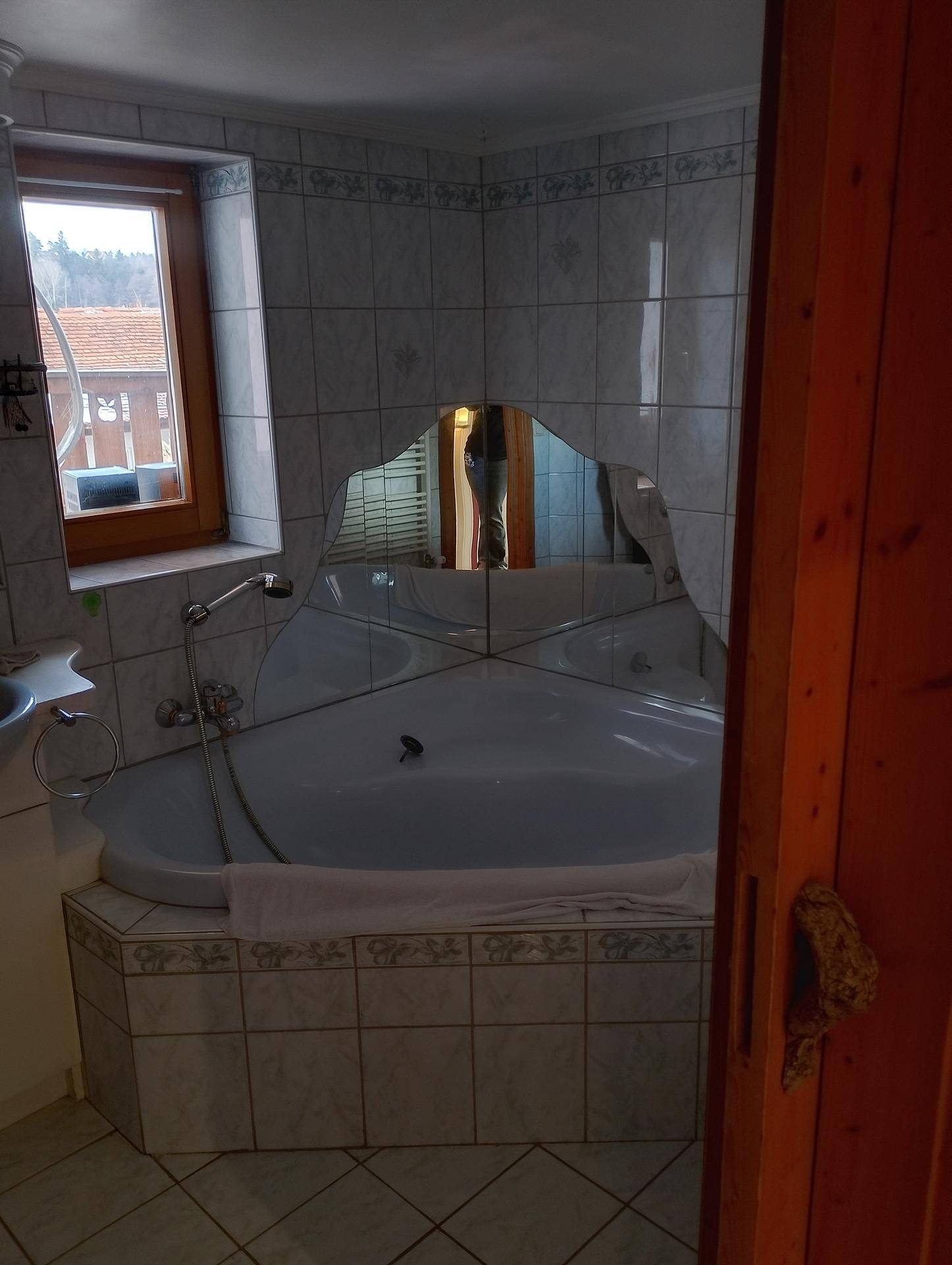 Badezimmer mit Eckbadewanne, gefliesten Wänden und einem Fenster für Tageslicht.