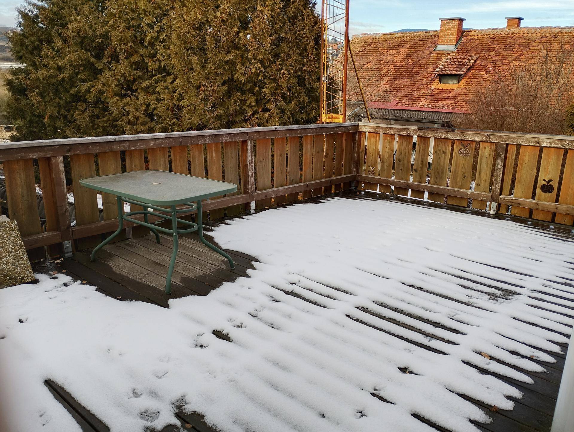 Holzterrasse mit Schnee bedeckt, einem kleinen Tisch und rustikalem Holzzaun.