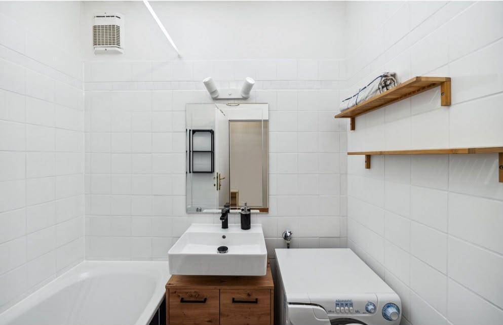 Helles Badezimmer mit Badewanne, modernem Waschbecken und Waschmaschine, komplett gefliest in Weiß.