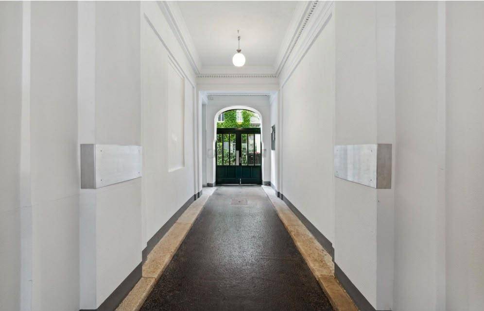 Langer, heller Hausflur mit klassischer Architektur und Blick auf eine grüne Eingangstür.
