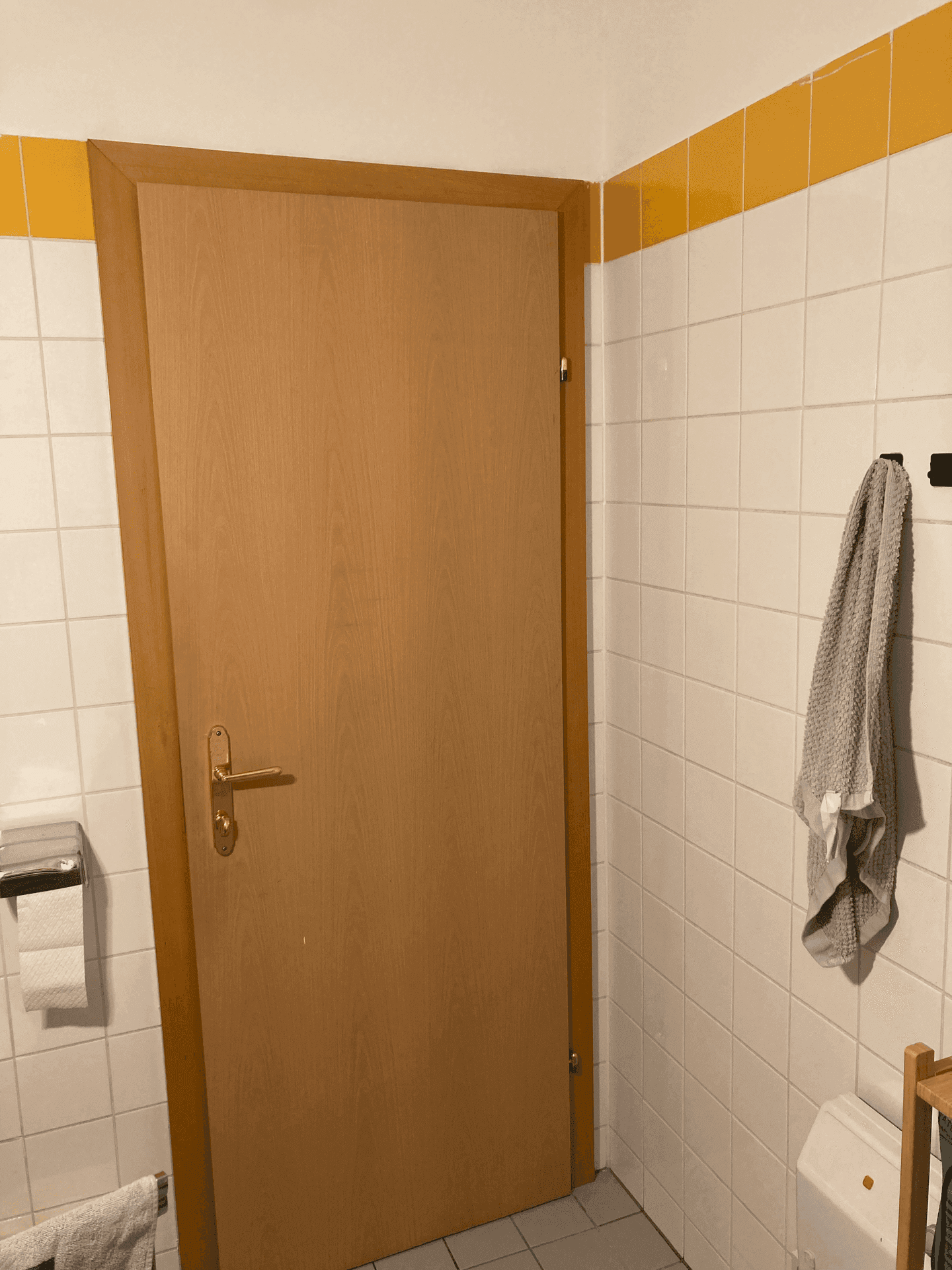 Separates WC mit Holztür, weißen Fliesen und gelbem Dekorstreifen an der Wand.