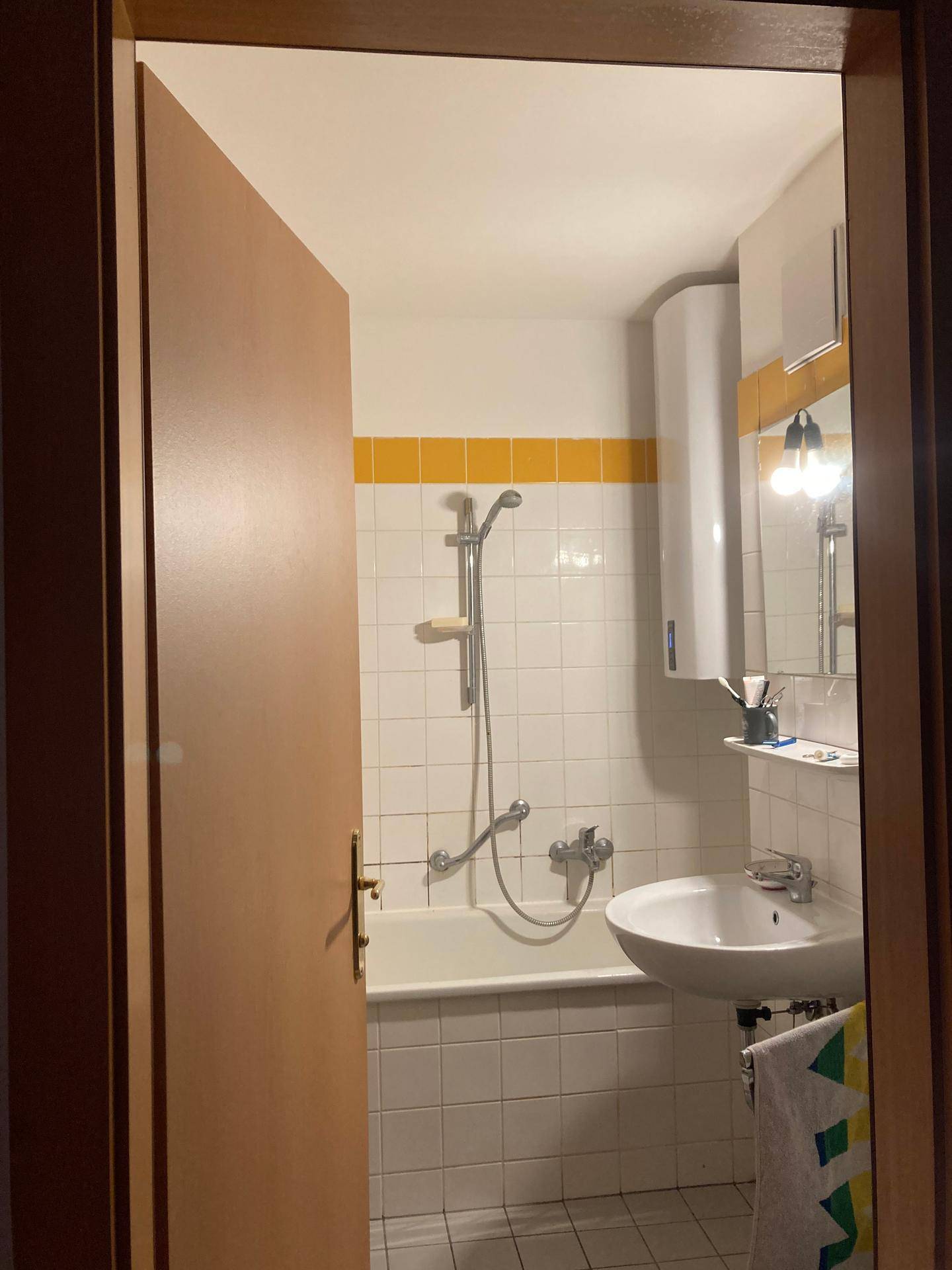 Badezimmer mit Badewanne, Duschfunktion, Waschbecken und Spiegelschrank, gelbe Akzente.