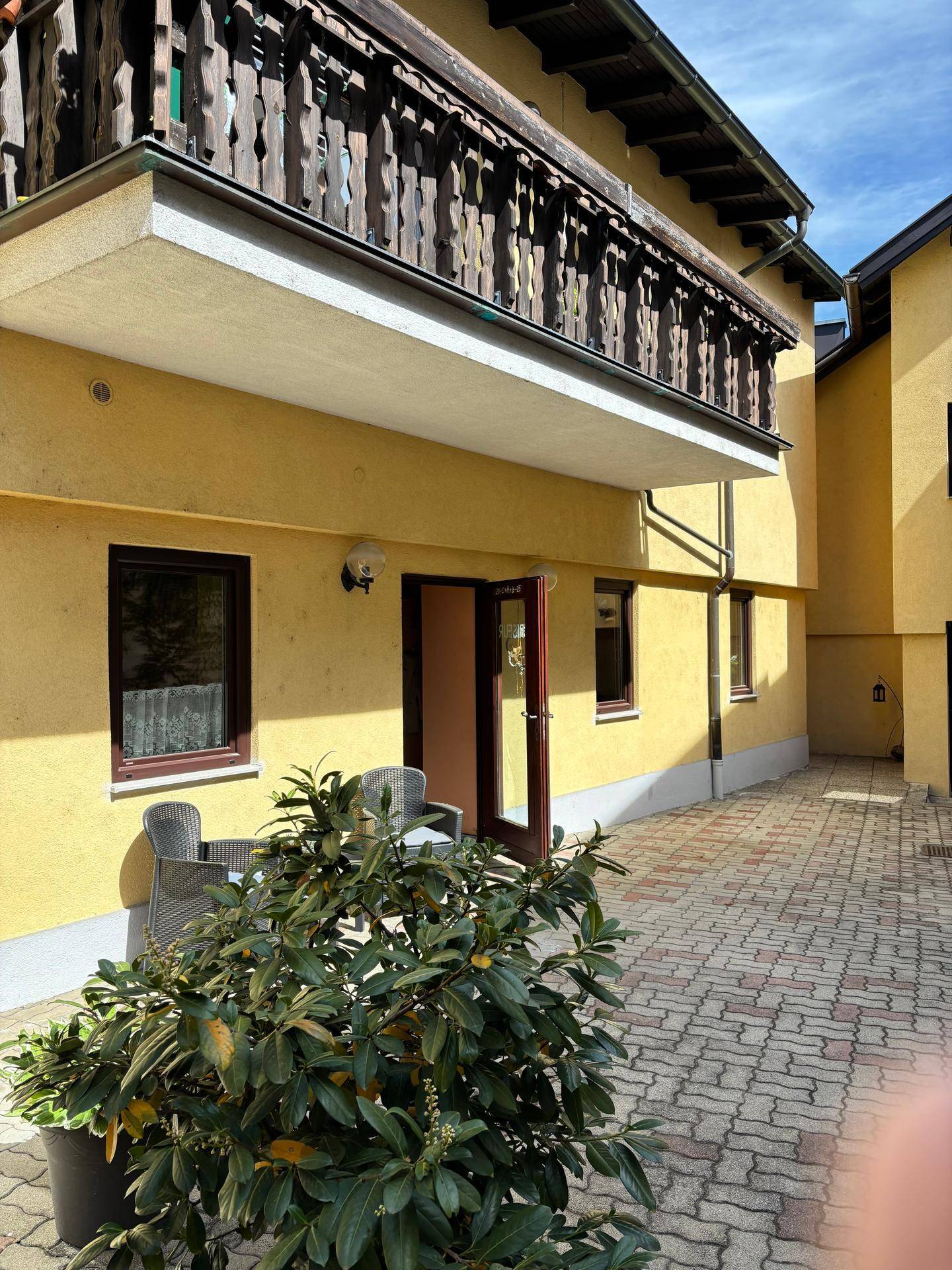Ein sonniger Innenhof mit Sitzgelegenheiten und einem traditionellen Holzbalkon am gelben Gebäude.