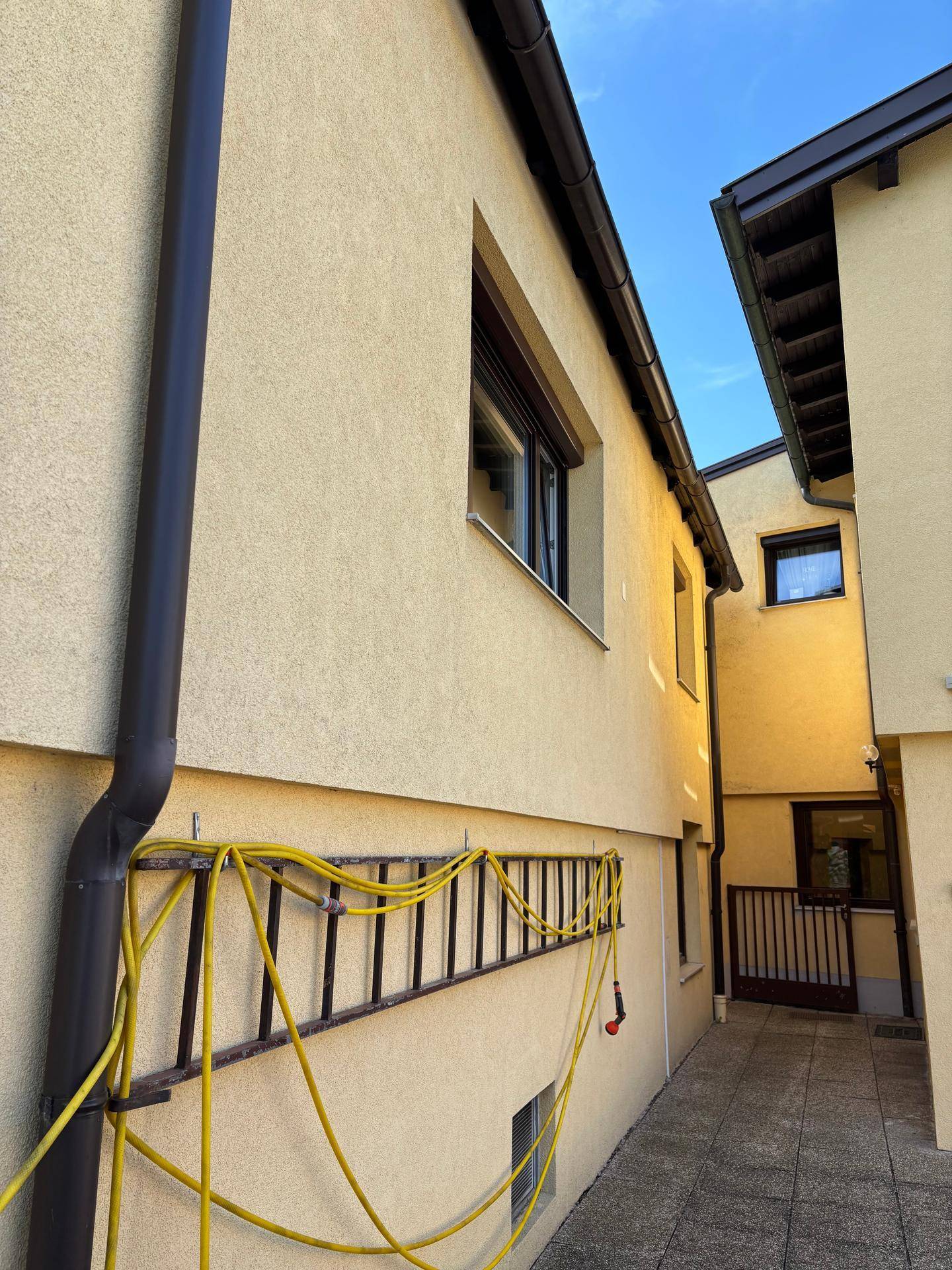 Seitenansicht eines gelben Gebäudes mit einem Fenster und einem Gartenschlauch an der Wand.