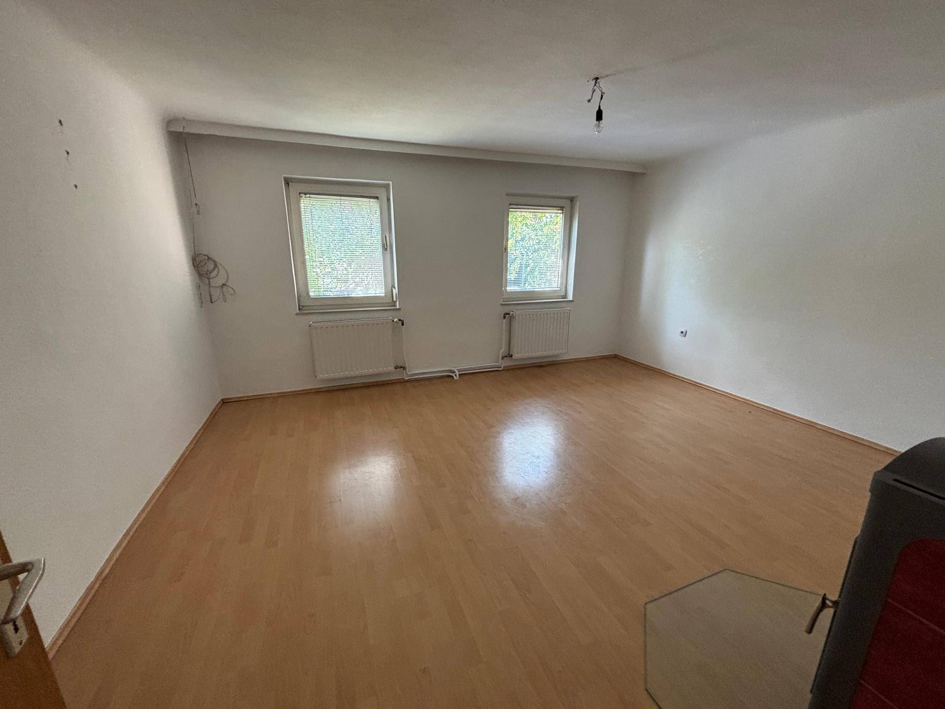 Geräumiges Zimmer mit Laminatboden, weißen Wänden und einem Holzofen in der Ecke.
