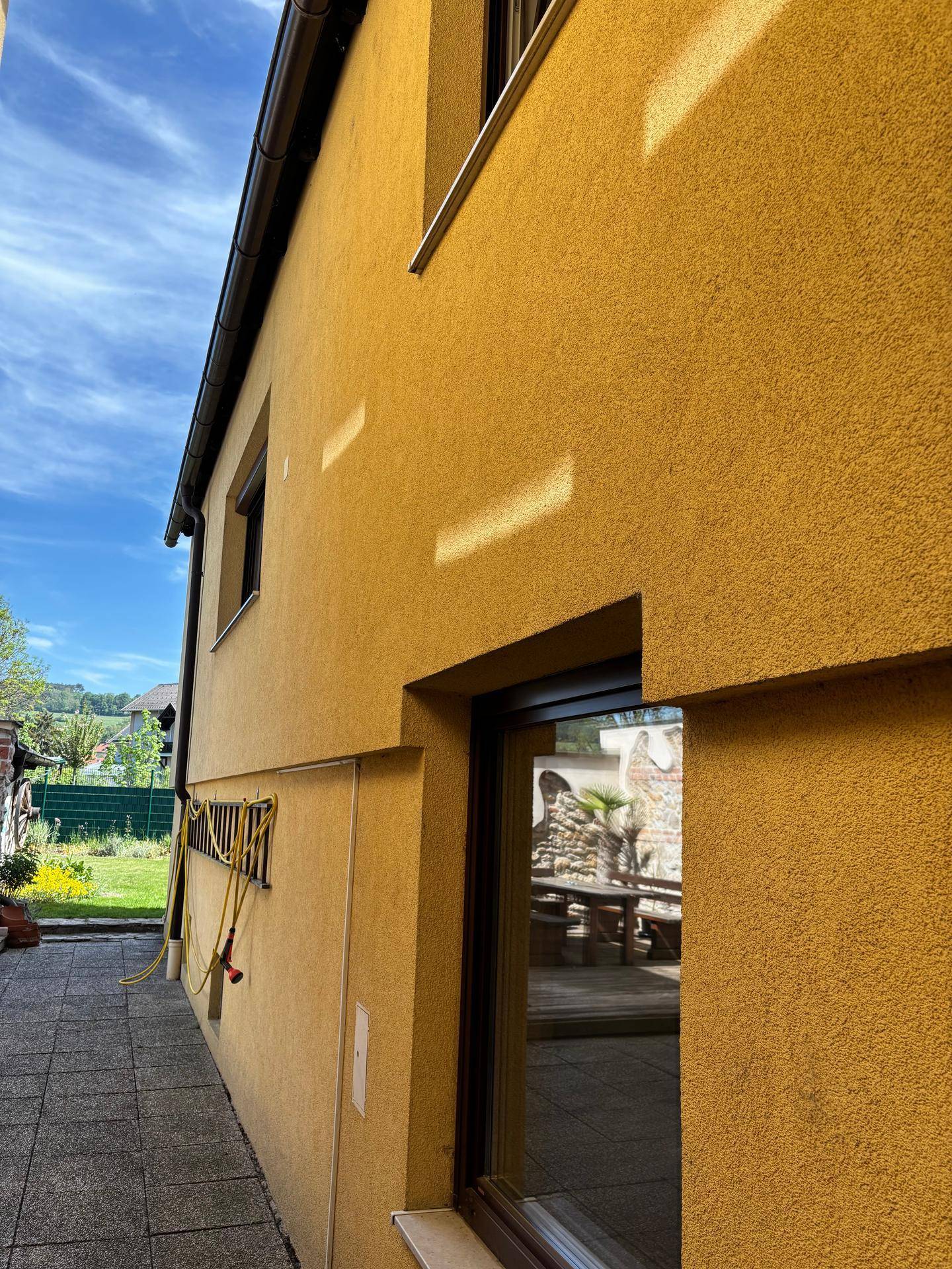 Seitenansicht eines gelben Gebäudes mit einem großen Fenster, das eine Terrasse widerspiegelt.