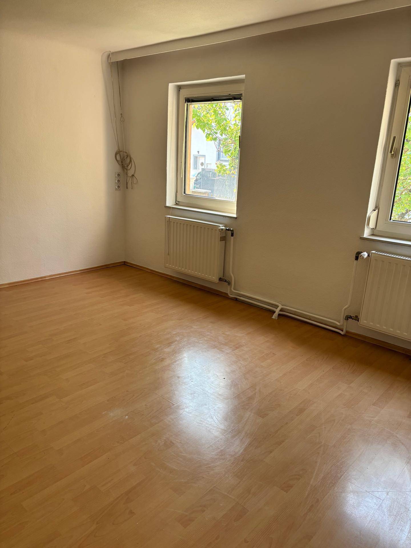 Helles Zimmer mit Laminatboden, weißen Wänden und zwei Fenstern, die viel Tageslicht hereinlassen.
