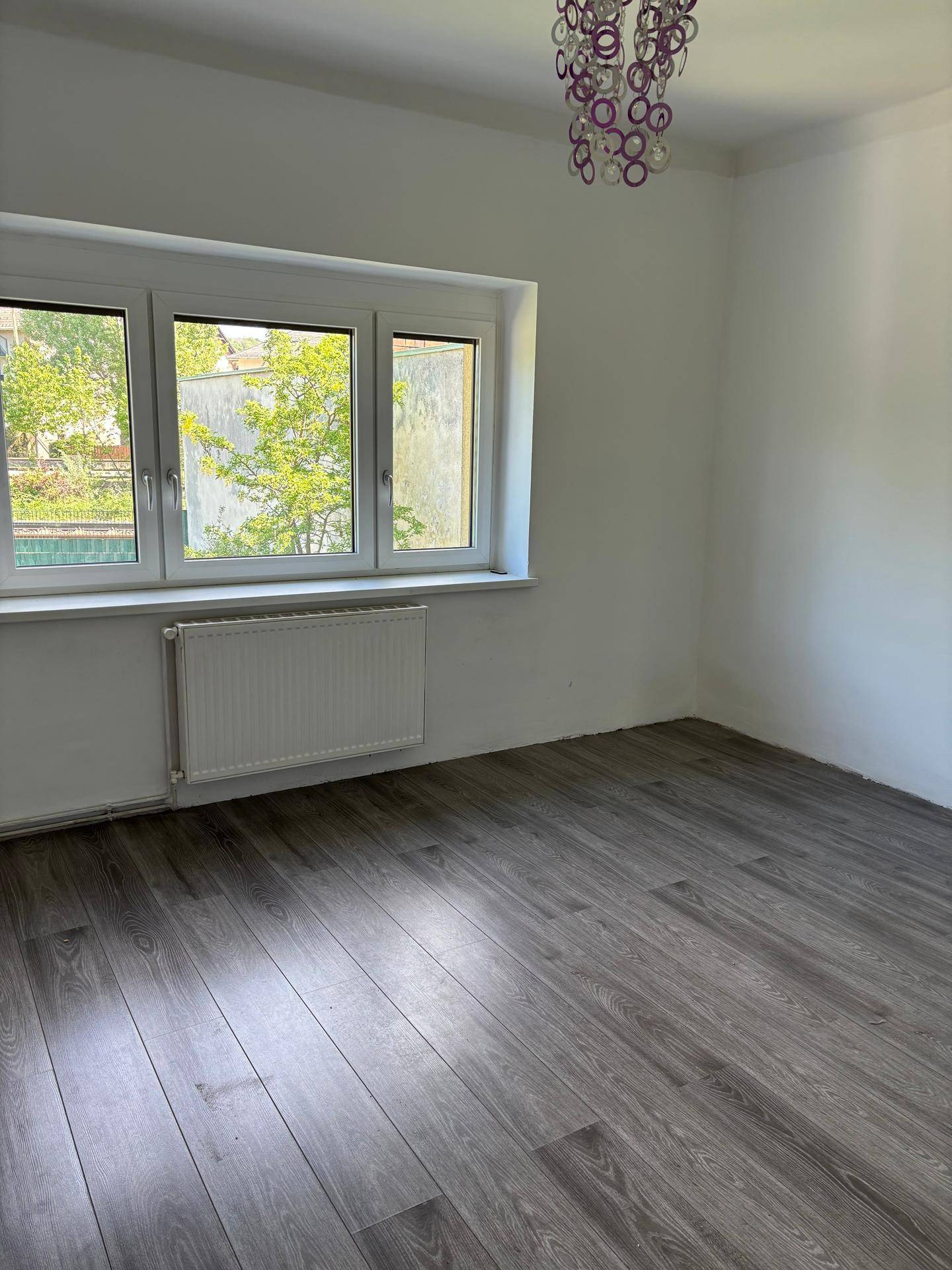 Ein helles Schlafzimmer mit grauem Laminatboden, weißen Wänden und einem großen Fenster.