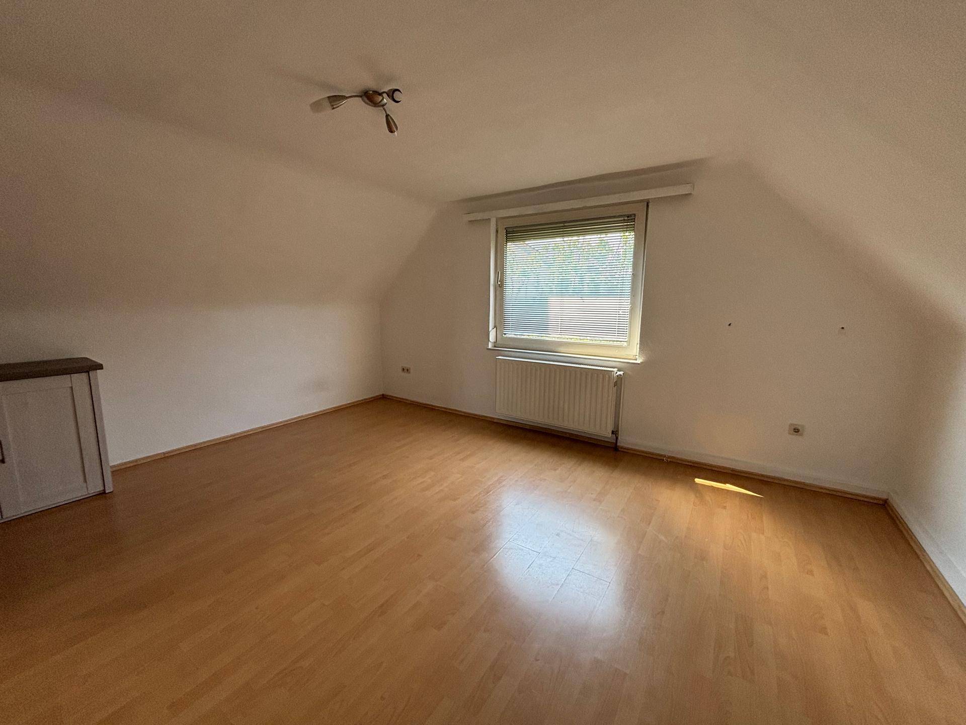 Dachgeschosszimmer mit Laminatboden, schrägen Wänden und einem Fenster mit Jalousien, gut beleuchtet.