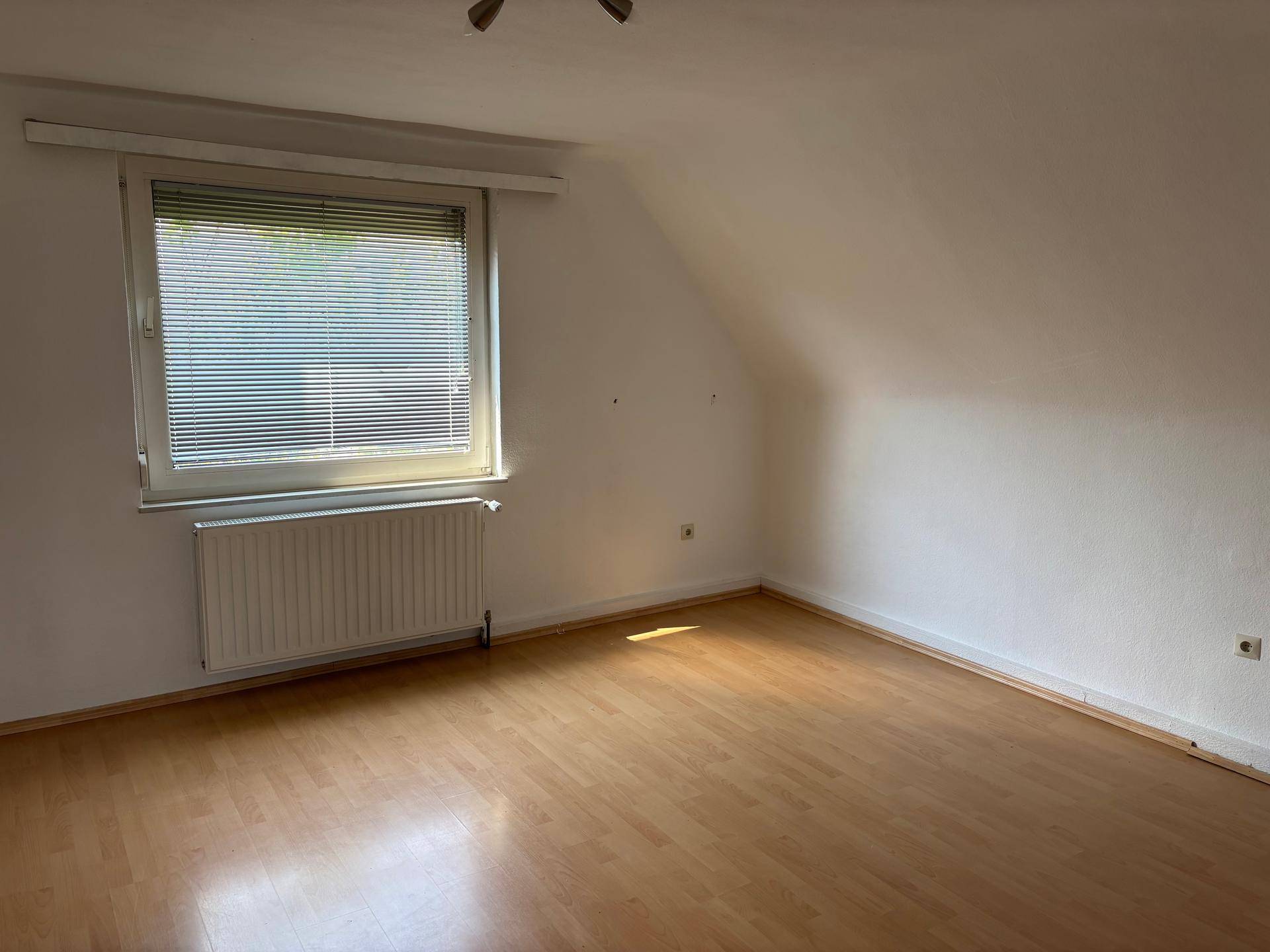 Helles Schlafzimmer im Dachgeschoss mit Laminatboden, schrägen Wänden und einem Fenster mit Jalousien.