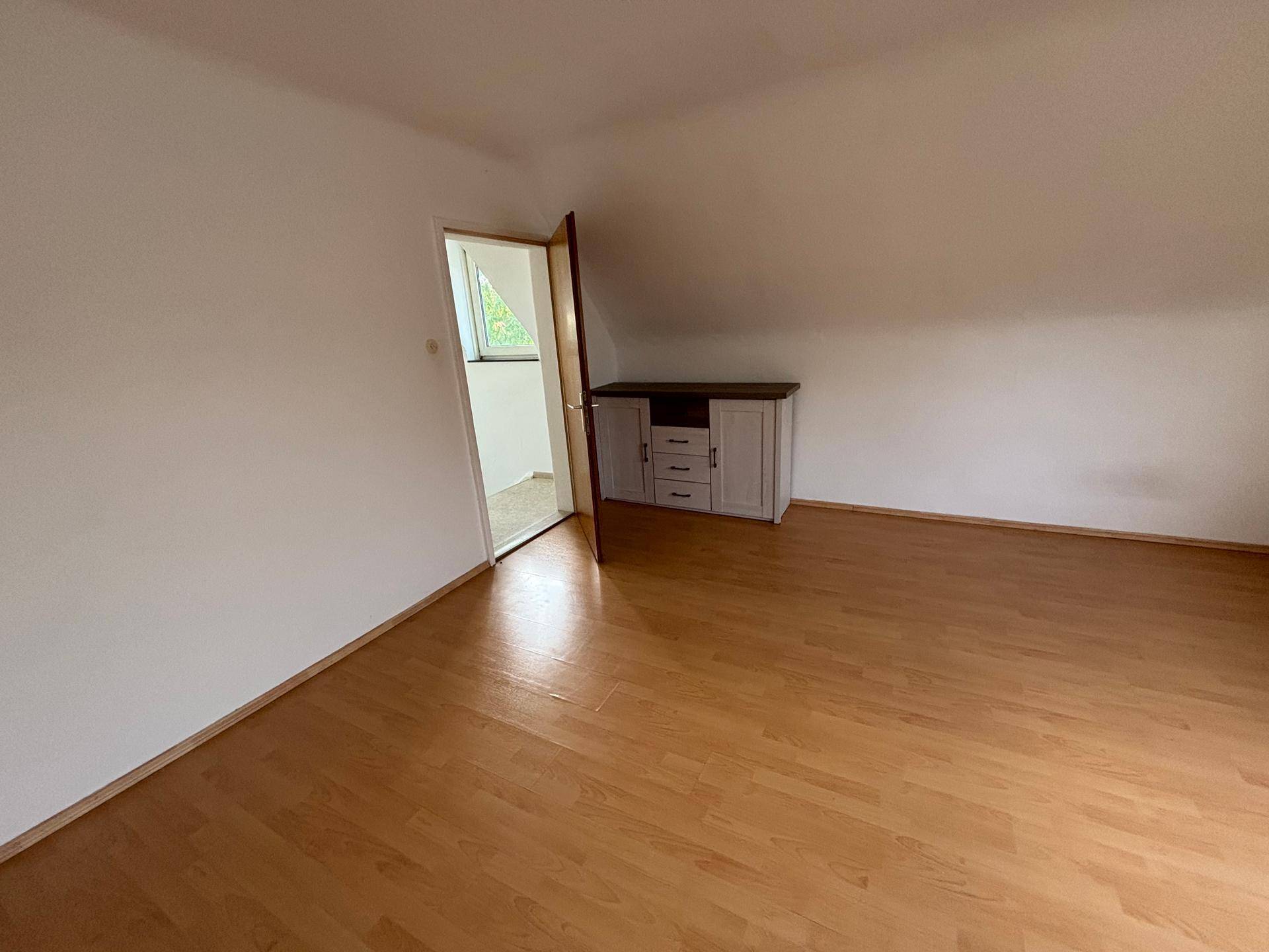 Dachgeschosszimmer mit Laminatboden, schrägen Wänden und einem Schrank, der viel Stauraum bietet.